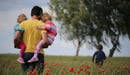 A dad carries his two daughters outside in a field. 